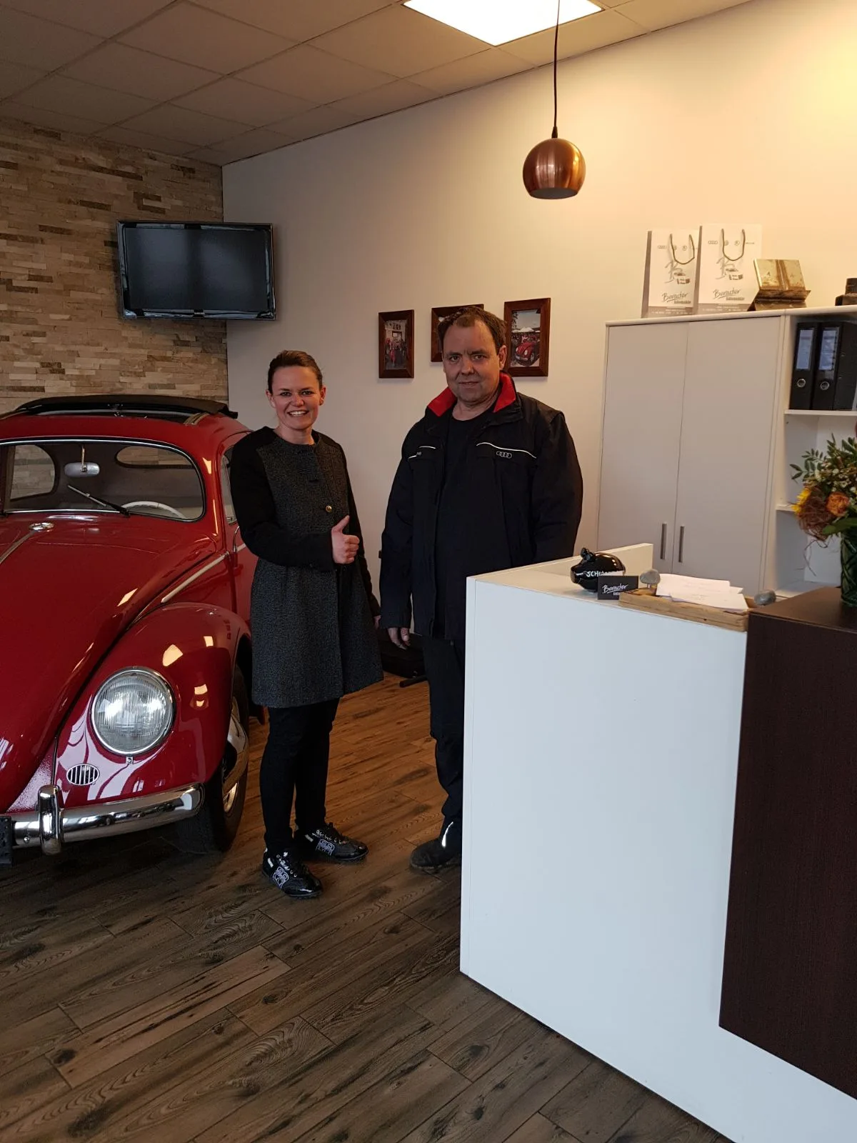 Mia und Josef Bereuter stehen im Schauraum neben einem roten VW Käfer